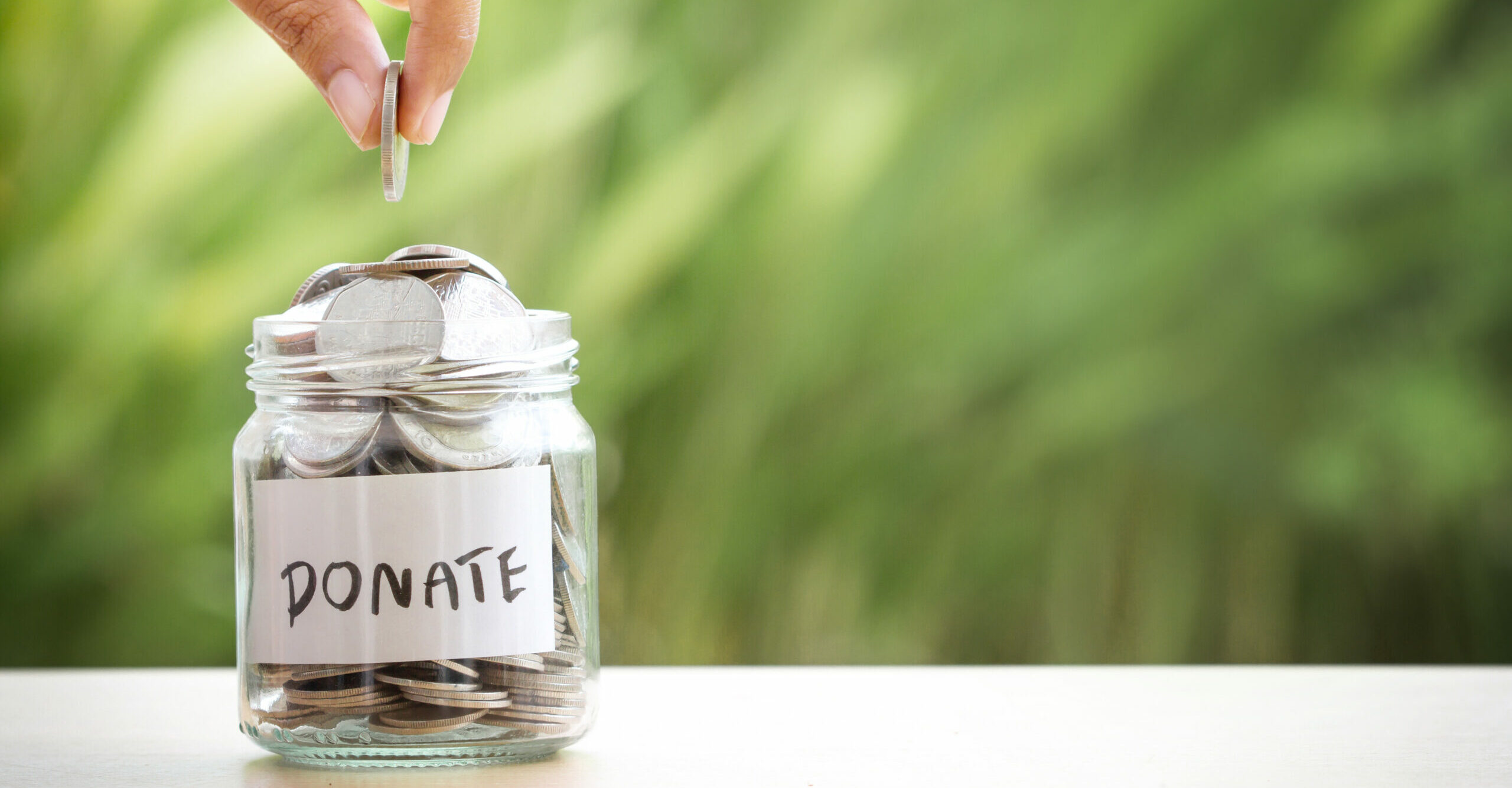 Hand putting Coins in glass jar for giving and donation concept