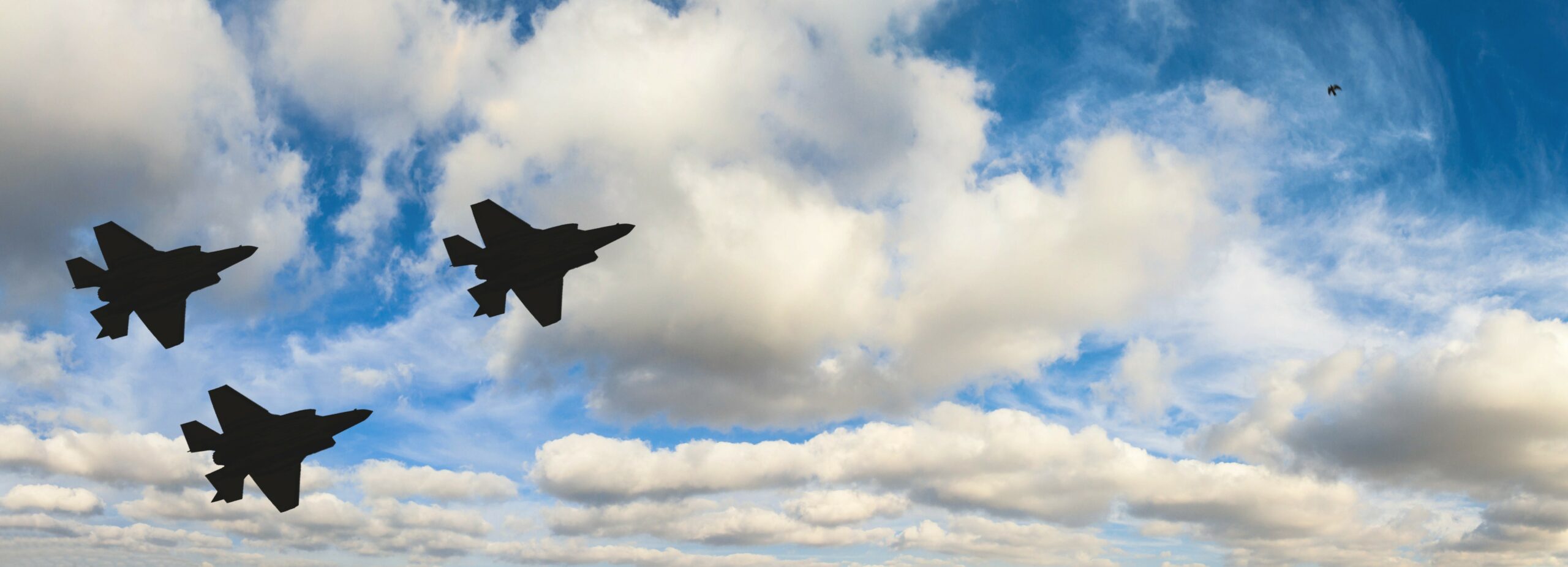 Silhouettes of three F-35 aircraft against the blue sky and white clouds